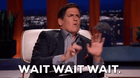 Man in a suit sitting in a chair gesturing with his hands as text on screen reads 'WAIT WAIT WAIT.'